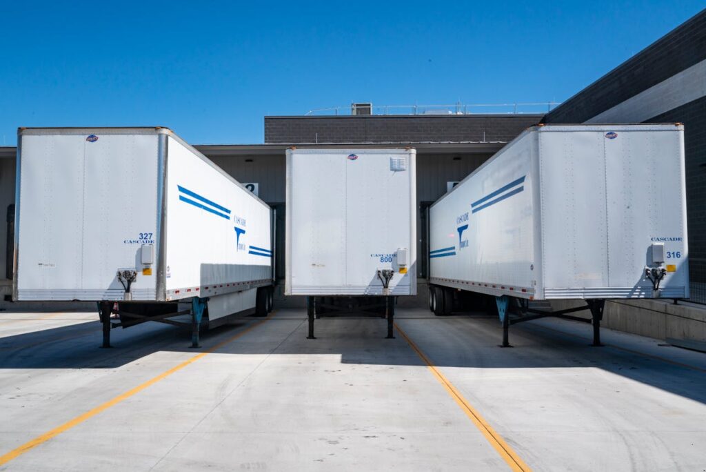 pexels-photo-1267325 Three white cargo trailers parked at an industrial shipping dock under clear blue skies.