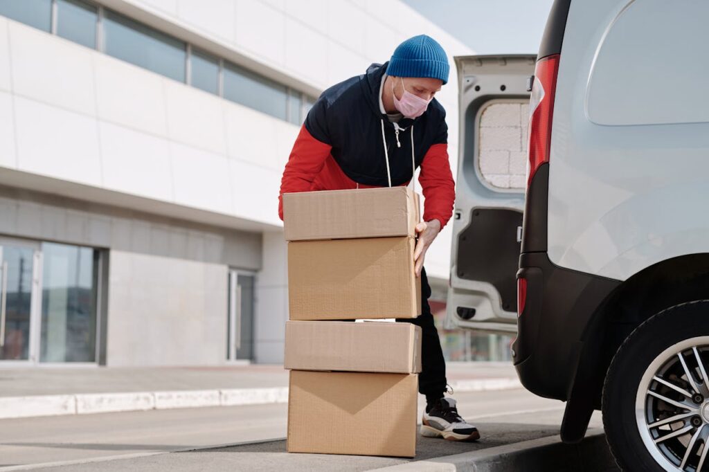 pexels-photo-4391478 Delivery worker wearing a face mask loads boxes into a van, reflecting pandemic precautions.