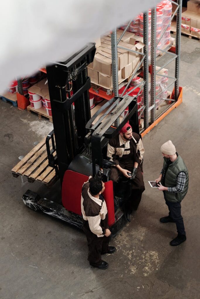 pexels-photo-4483561 Overhead view of warehouse workers having a meeting with forklift equipment. Collaborative workplace scenario.